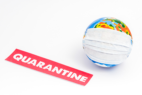 globe in medical mask near red paper with quarantine lettering on white with copy space