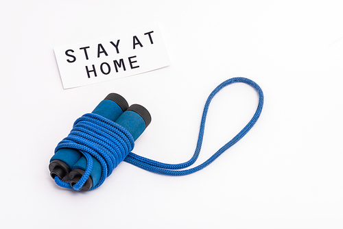 blue skipping rope near paper with stay at home lettering on white with copy space