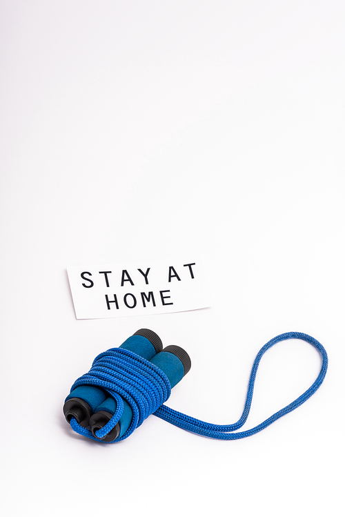 blue skipping rope near paper with stay at home lettering on white