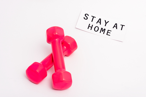 pink dumbbells near paper with stay at home lettering on white