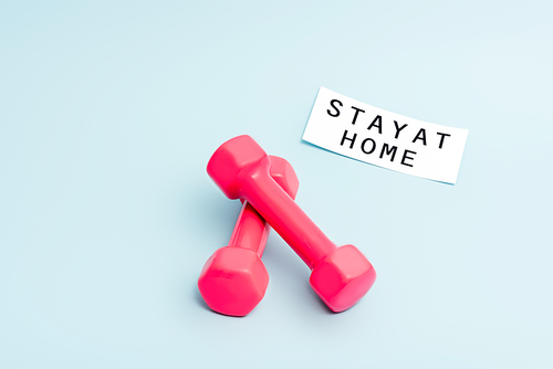 pink dumbbells near paper with stay at home lettering on blue with copy space