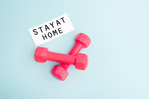 top view of pink dumbbells near paper with stay at home lettering on blue with copy space