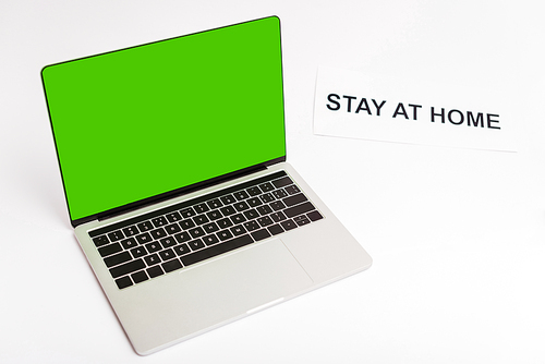 laptop with green screen near paper with stay at home lettering on white