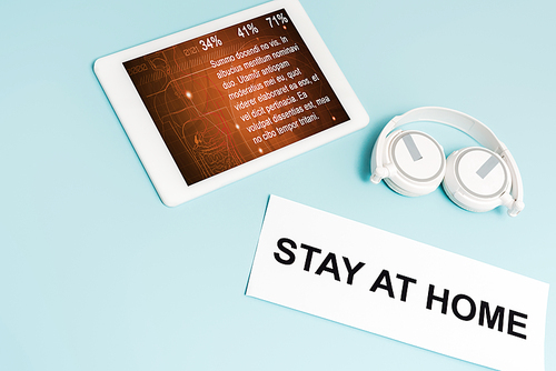 digital tablet with medical app near headphones and paper with stay at home lettering on blue