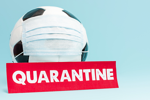 football in protective medical mask near red paper with quarantine lettering on blue