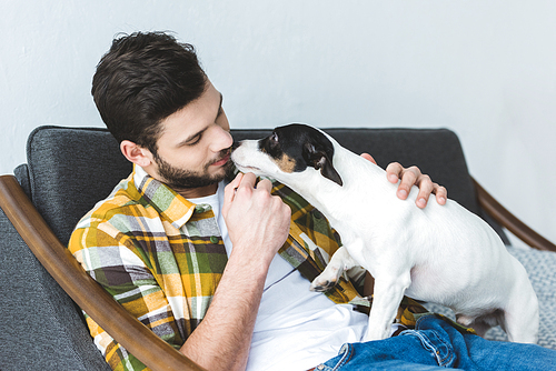 handsome man and jack russell terrier dog sitting on sofa at home