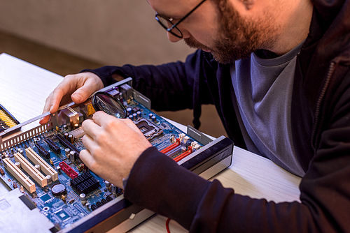 man in glasses fixing broken computer motherboard