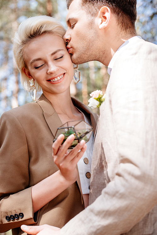 cropped view of bridegroom kissing bride with closed eyes