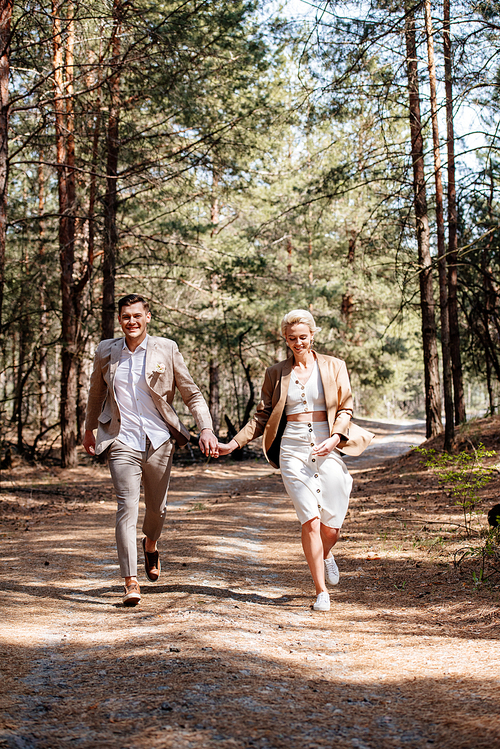 full length view of just married couple holding hands and walking in forest