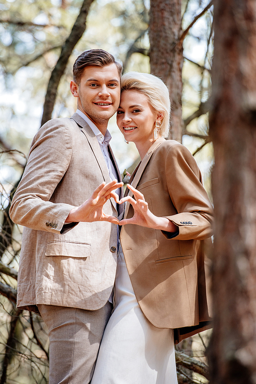 stylish smiling couple showing heart sign in forest