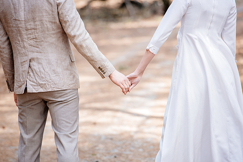 cropped view of just married couple holding hands in forest