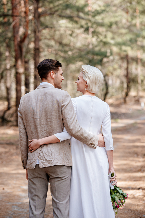 back view of just married couple embracing and looking at each other in forest