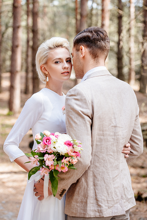 just married couple in formal wear embracing in forest
