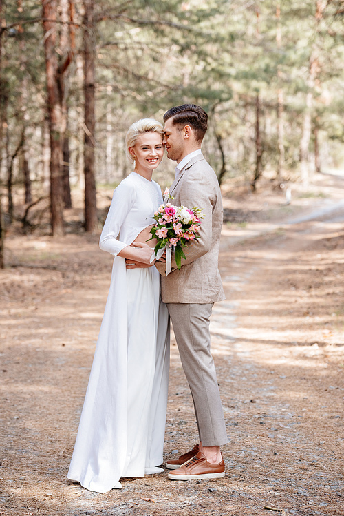 full length view of just married couple embracing in forest