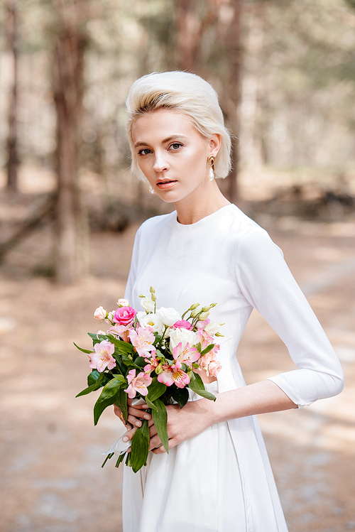 attractive blonde bride holding wedding bouquet in forest