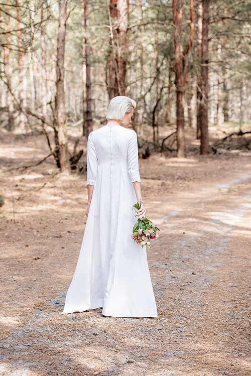 back view of blonde bride holding bouquet in forest