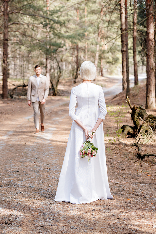 back view of bride with flowers and bridegroom in forest