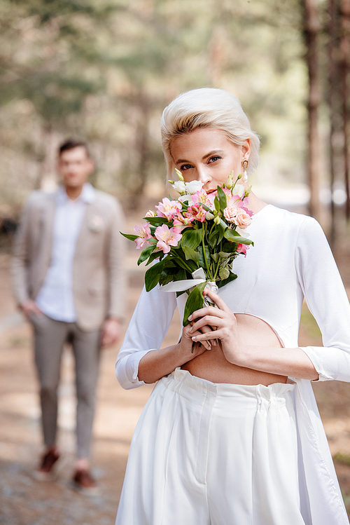 pretty bride with bouquet of flowers and bridegroom in forest