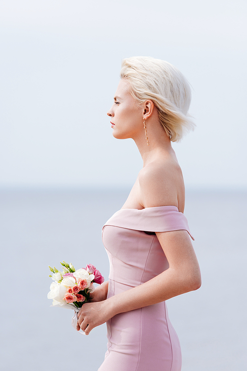 side view of pensive blonde girl in pink dress holding bouquet