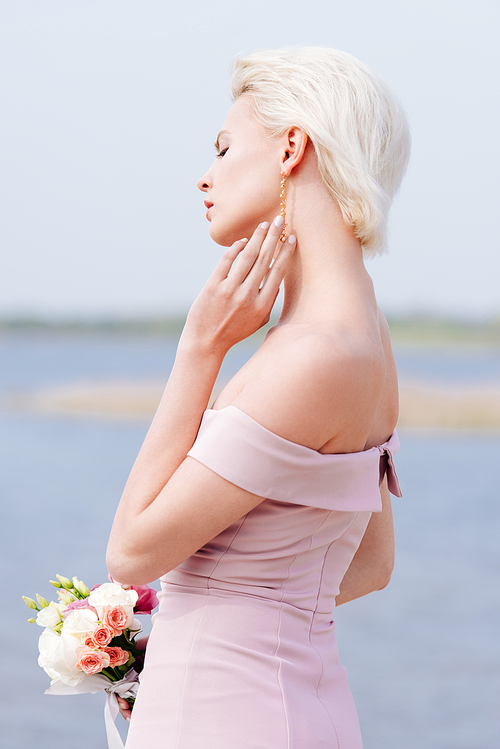 pensive blonde girl in pink dress holding bouquet