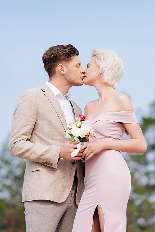 stylish couple holding wedding bouquet and kissing with closed eyes