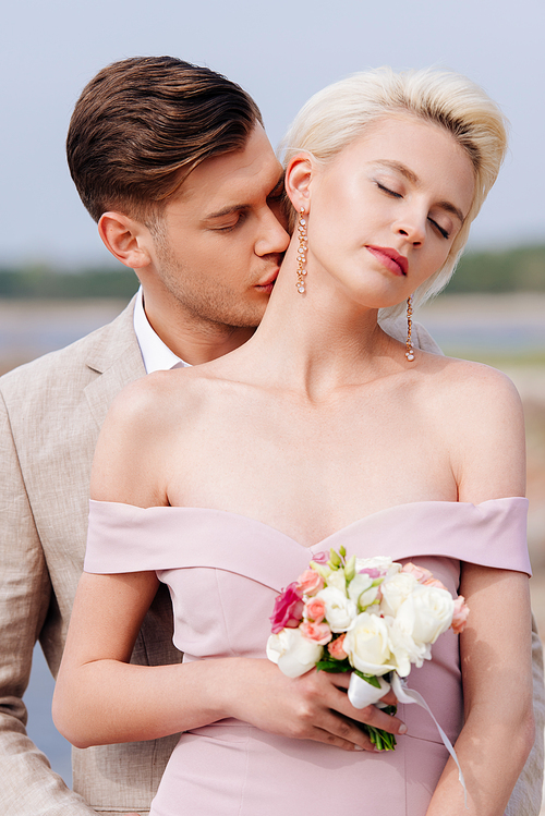 stylish bridegroom kissing bride in neck with closed eyes