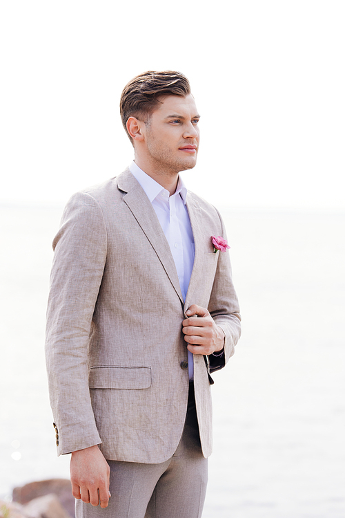 dreamy bridegroom in formal wear with pink boutonniere looking away