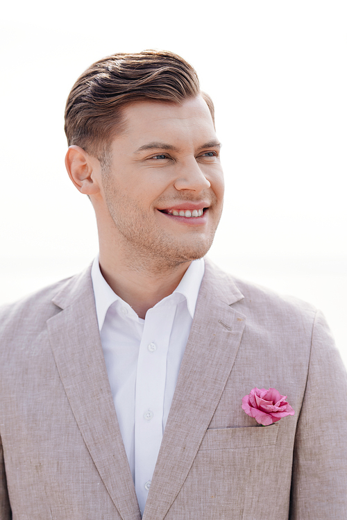 stylish smiling bridegroom in formal wear with boutonniere looking away