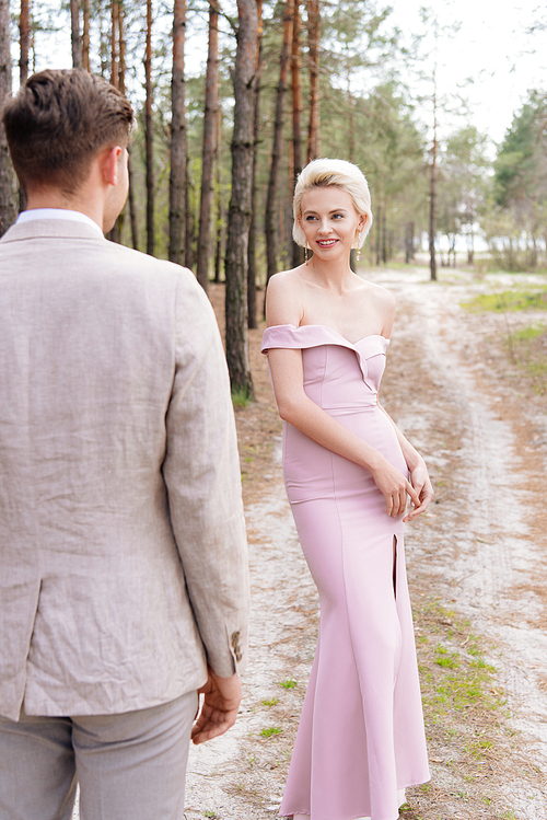 smiling girl in pink dress looking at bridegroom in forest