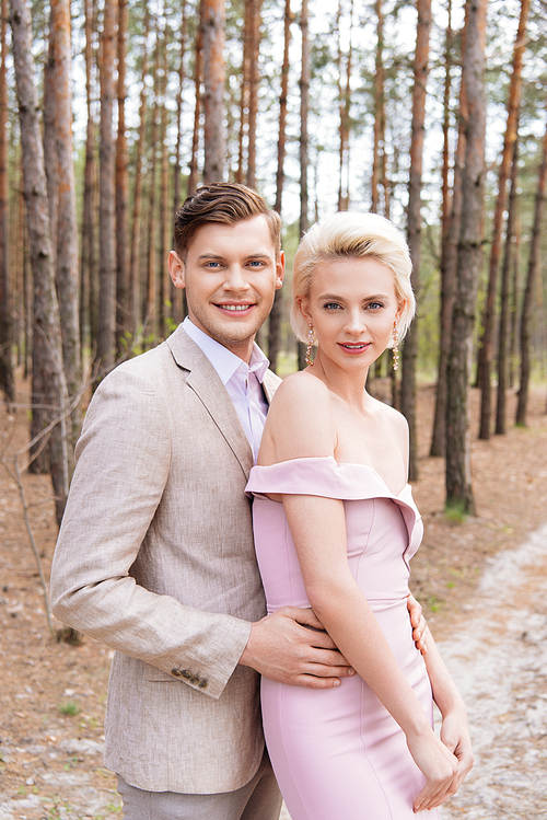 happy just married couple embracing in forest with smile