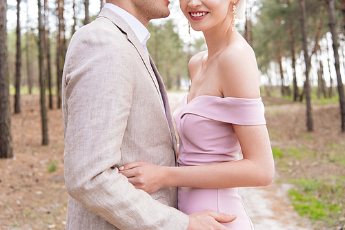 cropped view of happy just married couple embracing in forest with smile