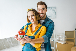 Smiling couple holding toy house and  at home