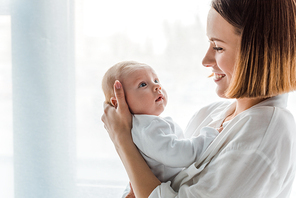 Smiling mother in white shirt holding baby at home