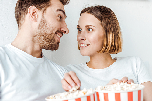 smiling couple with popcorn looking at each other at home