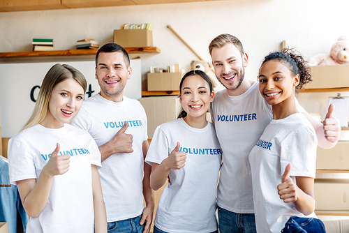 five young multicultural volunteers showing thumbs up, smiling and 