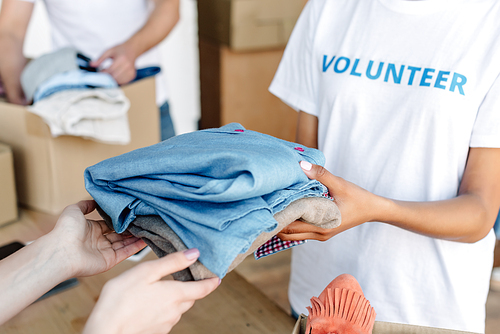 cropped view of volunteer giving clothes to woman in charity center