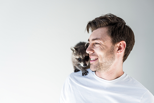 handsome smiling man with cute raccoon on shoulder on grey
