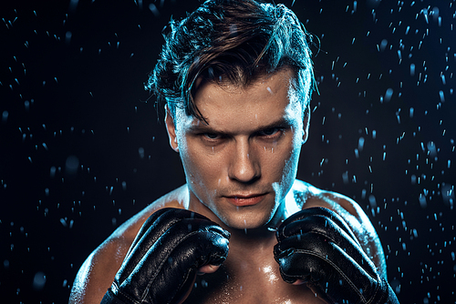 Front view of boxer in leather gloves standing under water drops on black