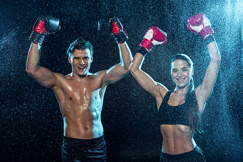 Two boxers in boxing gloves smiling and showing yes gestures under water drops on black