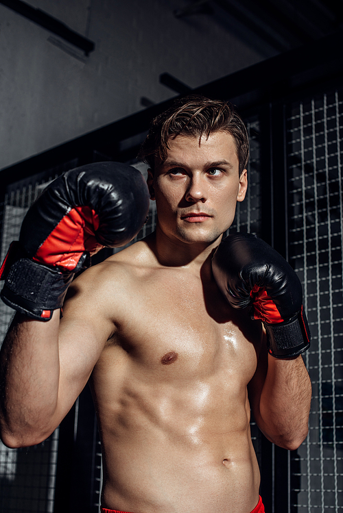 Pensive boxer in black boxing gloves holding hands up looking away