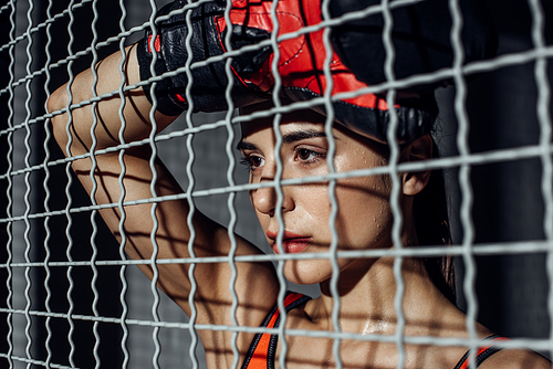 Attractive boxer standing behind wire netting and looking away