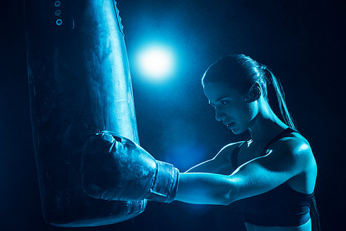 Confident female boxer with ponytail training with punching bag