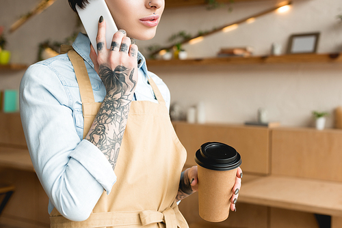 cropped view of waitress talking on smartphone and holding disposable cup