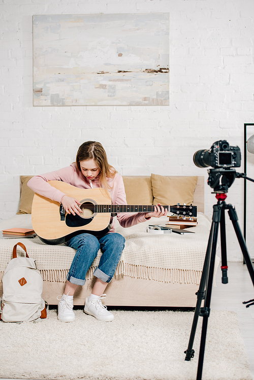 teenage . sitting on bed and playing acoustic guitar in front of camera