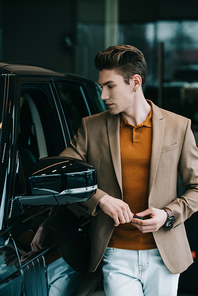 handsome man looking at black automobile in car showroom