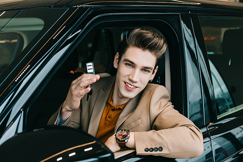 cheerful man sitting in automobile and holding car key while 