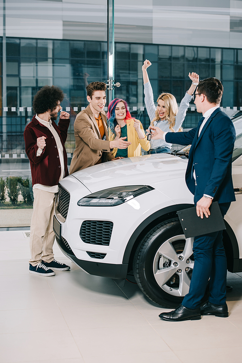 car dealer giving key to cheerful friends standing near white car
