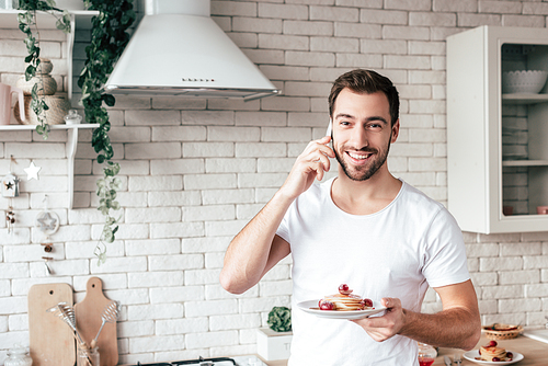 smiling man talking on smartphone and holding plate with pancakes