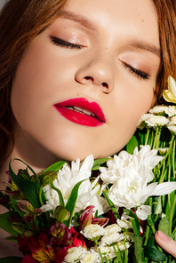 close up of beautiful young redhead woman with red lips and eyes closed posing with flowers