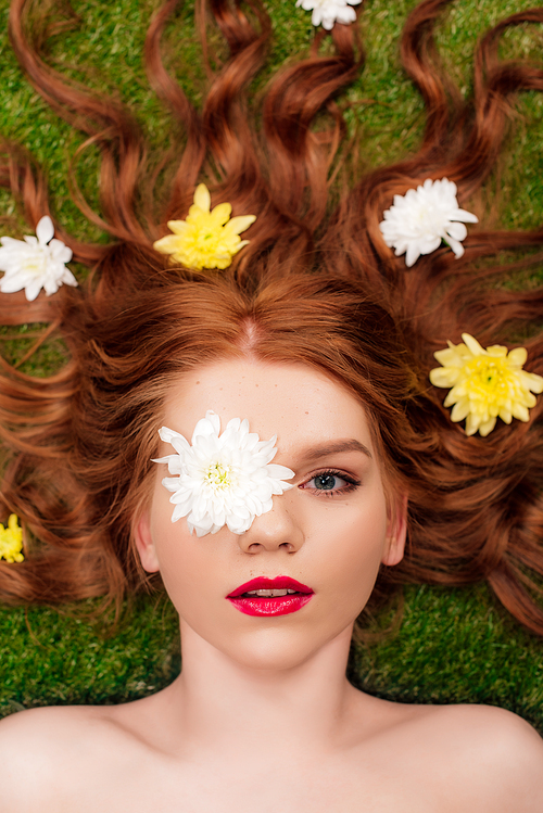 top view of beautiful young woman with red lips and chrysanthemum flowers in hair on grass